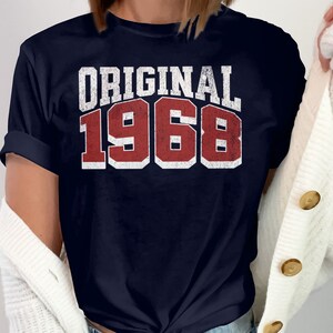 May include: A navy blue t-shirt with the text "ORIGINAL 1968" in white and red lettering.