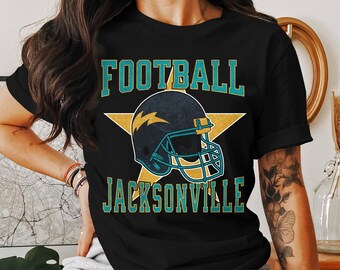 May include: Black t-shirt featuring a teal and yellow star with a football helmet graphic. The text "FOOTBALL JACKSONVILLE" is printed on the shirt.