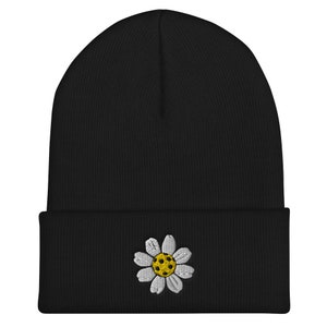 May include: Black beanie with a white daisy embroidered on the front. The daisy has a yellow center.