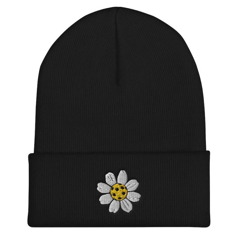 May include: Black beanie with a white daisy embroidered on the front. The daisy has a yellow center.