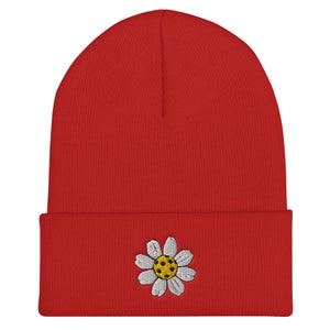 May include: Red beanie with a white daisy embroidered on the front. The daisy has a yellow center.