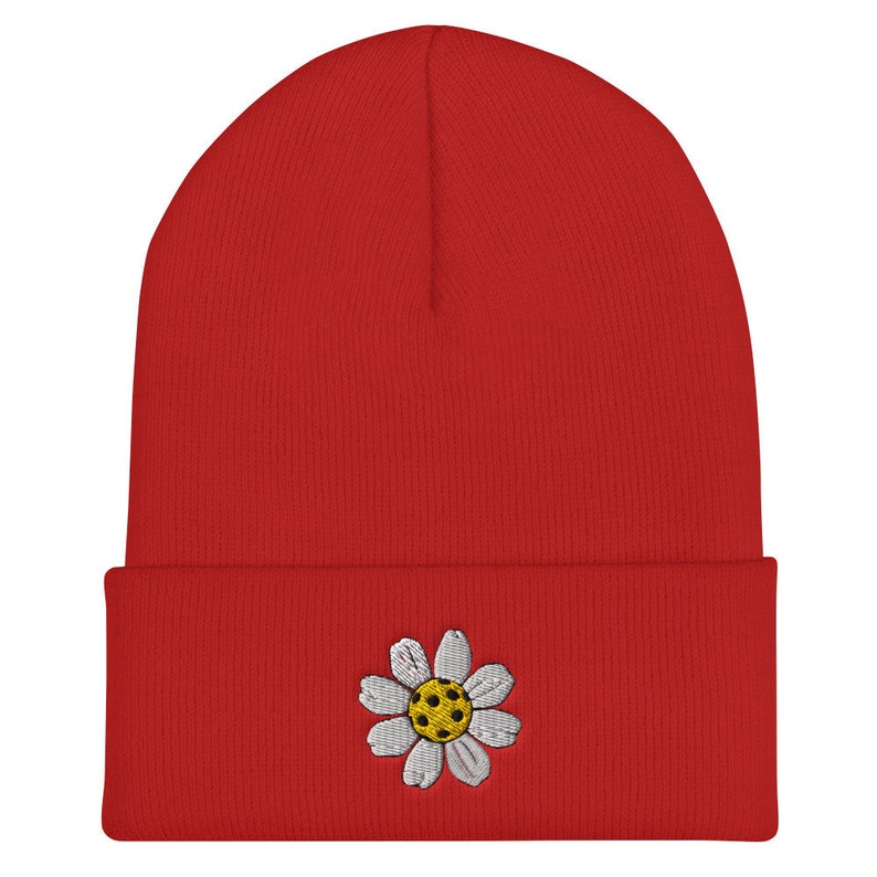 May include: Red beanie with a white daisy embroidered on the front. The daisy has a yellow center.