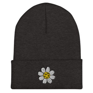 May include: A dark gray beanie with a white daisy embroidered on the front. The daisy has a yellow center.