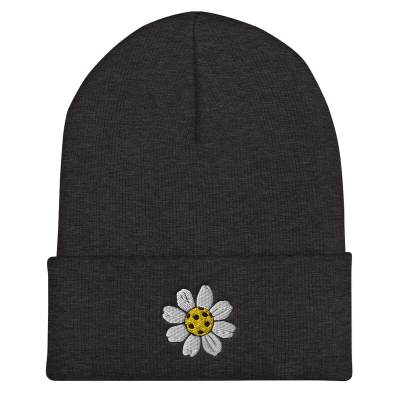 May include: A dark gray beanie with a white daisy embroidered on the front. The daisy has a yellow center.
