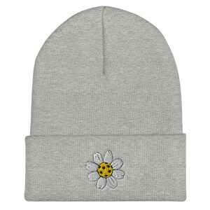 May include: Gray beanie with a white daisy embroidered on the front. The daisy has a yellow center.