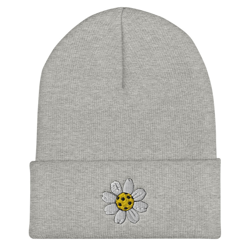 May include: Gray beanie with a white daisy embroidered on the front. The daisy has a yellow center.
