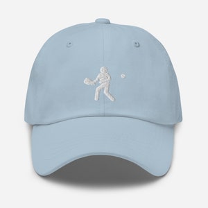 Puede incluir: Una gorra de b&eacute;isbol azul claro con una silueta de jugador de b&eacute;isbol bordada en blanco.