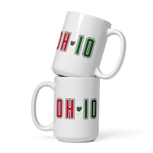 May include: Two white ceramic mugs stacked on top of each other. Each mug has the letters "OH-IO" in red and green, with a gray outline of the state of Ohio. The mugs have large handles.