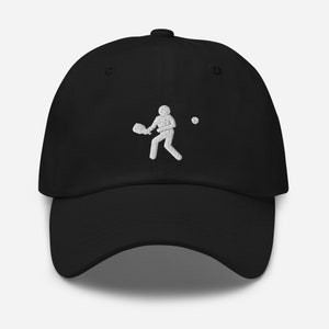 Puede incluir: Una gorra de b&eacute;isbol negra con una imagen bordada en blanco de una persona jugando un deporte con una raqueta y una pelota.