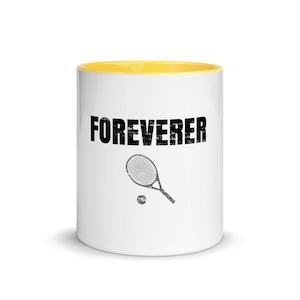 May include: White ceramic coffee mug with a yellow rim. The mug features a black tennis racket and ball graphic with the text "FOREVERER" in black.