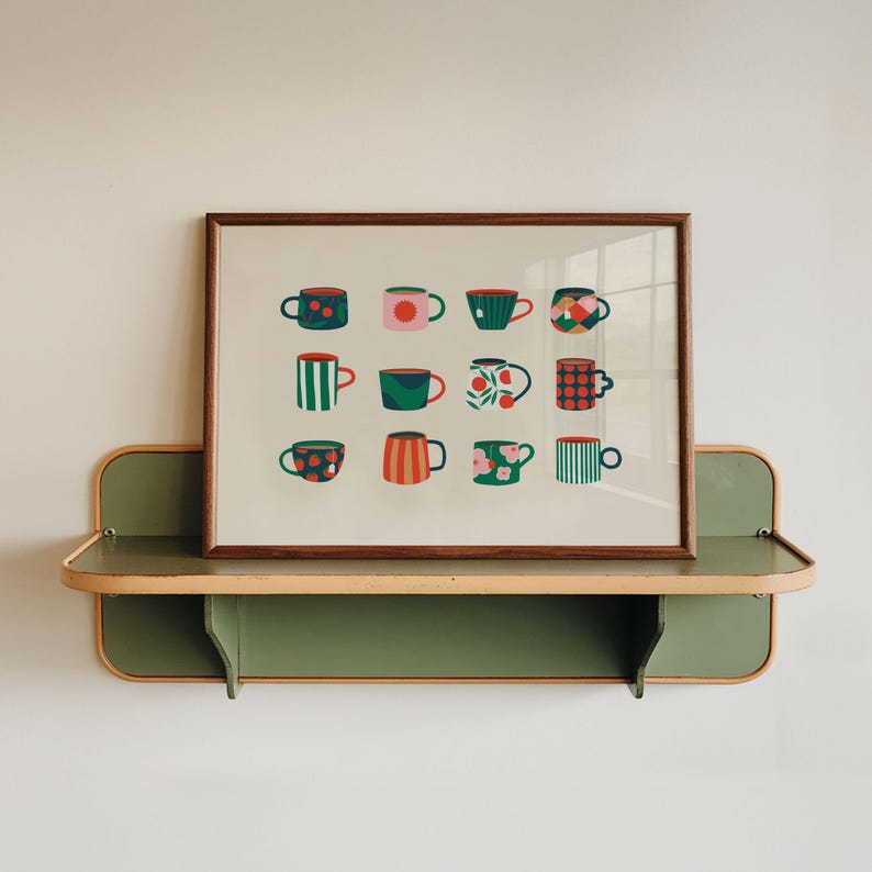 May include: A framed print featuring a grid of twelve colorful coffee cups with various patterns, including stripes, polka dots, and floral designs. The print is displayed on a green and wood-toned shelf against a white wall.