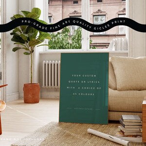 K&ouml;nnte beinhalten: Ein gerahmter Kunstdruck mit tealfarbenem Hintergrund zeigt den Text: "YOUR CUSTOM QUOTE OR LYRICS WITH A CHOICE OF 45 COLOURS." Der Druck befindet sich in einem Raum mit Sofa, Pflanze und Holzstuhl. Der Text "PRO-GRADE FINE ART QUALITY GICLEE PRINT" steht oben.