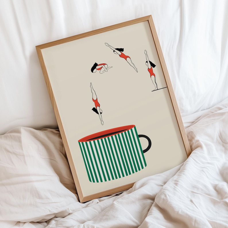 May include: A framed art print featuring a whimsical illustration. The artwork depicts stylized figures in red swimsuits diving into a large coffee mug with green and white stripes. The mug has a red rim and a black handle.