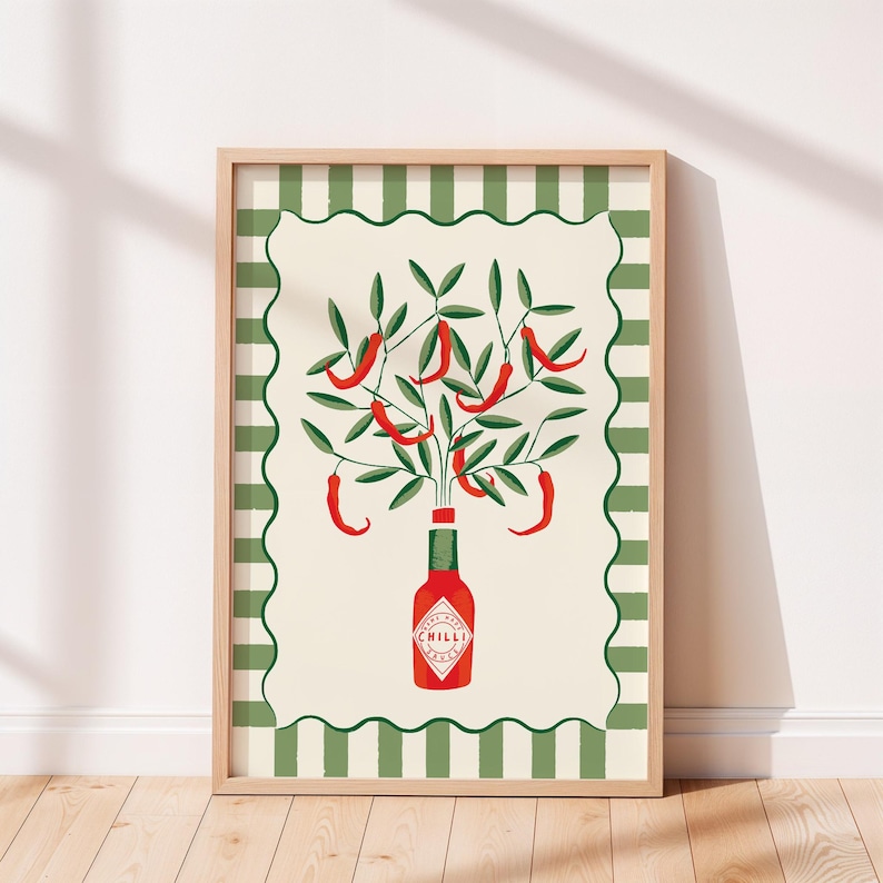 May include: A framed art print featuring a stylized illustration of a red chili pepper plant. The plant sprouts from a red bottle labeled "CHILLI" against a cream background with a green and white striped border. The frame is light brown.