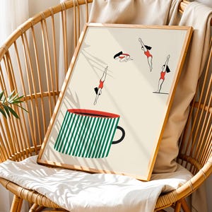 May include: A framed art print featuring a whimsical illustration of divers in red swimsuits and a large green and white striped coffee mug. The artwork is displayed on a light beige background and is set in a natural wood frame.