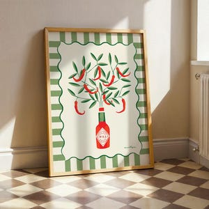 May include: A framed art print featuring a stylized illustration of red chili peppers growing from a green bottle labeled "Chilli". The artwork has a cream background with a green and white border, and is set in a wooden frame.