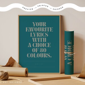 May include: A framed teal print with the text "YOUR FAVOURITE LYRICS WITH A CHOICE OF 30 COLOURS." A rolled teal poster with text is next to the framed print. Brown paper and twine are also in the image.