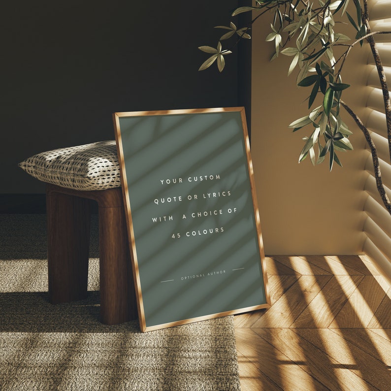 K&ouml;nnte beinhalten: Ein gerahmter Druck mit goldenem Rahmen lehnt an einem Holzschemel. Der Druck hat einen dunkelgr&uuml;nen Hintergrund mit wei&szlig;em Text, der lautet: "YOUR CUSTOM QUOTE OR LYRICS WITH A CHOICE OF 45 COLOURS". Ein Kissen und eine Pflanze befinden sich im Hintergrund.