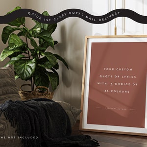 K&ouml;nnte beinhalten: Ein gerahmter Druck mit terrakottafarbenem Hintergrund und dem Text "YOUR CUSTOM QUOTE OR LYRICS WITH A CHOICE OF 45 COLOURS". Der Rahmen ist aus hellem Holz. Eine gro&szlig;e gr&uuml;ne Pflanze und ein graues Sofa sind im Hintergrund. Der Text oben lautet "QUICK 1ST CLASS ROYAL MAIL DELIVERY".