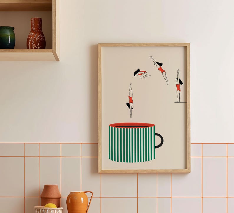 May include: A framed art print featuring a whimsical design. The artwork depicts stylized figures in red swimsuits diving into a large green and white striped coffee cup. The cup has a red rim and a black handle. The background is a light beige.