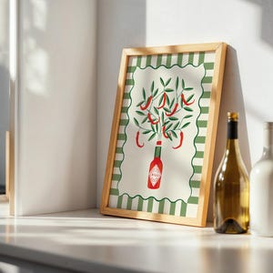 May include: A framed art print featuring a stylized illustration of a Tabasco sauce bottle with chili peppers and green leaves. The print has a green and white striped border and a natural wood frame. A wine bottle and glass are next to the frame.