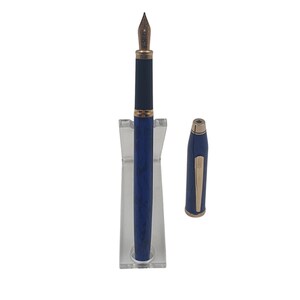 K&ouml;nnte beinhalten: Ein blau-goldener F&uuml;llfederhalter mit passender Kappe. Der Stift wird auf einem transparenten St&auml;nder pr&auml;sentiert, wobei die Kappe zur Seite gelegt ist. Der Stift hat eine goldene Feder und Akzente.