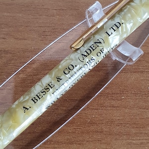 Może przedstawiać: Złoty i biały długopis z nadrukiem "A. Besse & Co. (Aden) Ltd. Distributors of Willys-Overland Jeeps" na boku.
