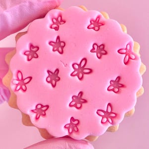 May include: A pink sugar cookie decorated with a pattern of small pink flowers.
