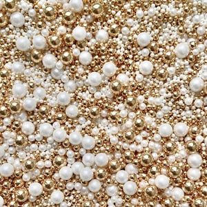 May include: A close-up image of a mixture of white and gold pearl sprinkles. The sprinkles are ideal for decorating cakes, cupcakes, and other desserts.