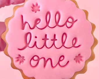 May include: Pink sugar cookie with white frosting and the words "hello little one" in pink icing.