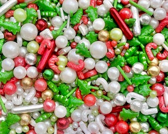 May include: A close-up of a mix of Christmas-themed sprinkles. The sprinkles include white, red, green, and gold shapes, including candy canes, tree shapes, and round and rod-shaped sprinkles. The sprinkles are a mix of sizes and textures.