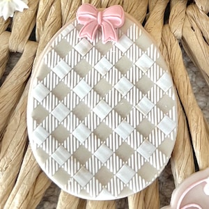 May include: A light brown and white checkered Easter egg cookie with a pink bow on top.