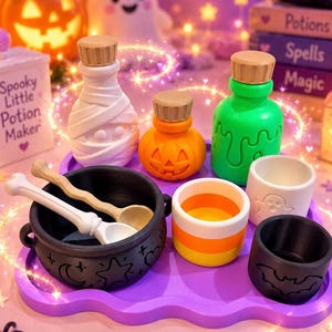 May include: A Halloween-themed set featuring a black cauldron with celestial symbols, two bone-shaped spoons, a mummy-shaped bottle, a pumpkin-shaped bottle, a green slime bottle, a candy corn cup, a ghost cup, and a bat cup on a purple tray.