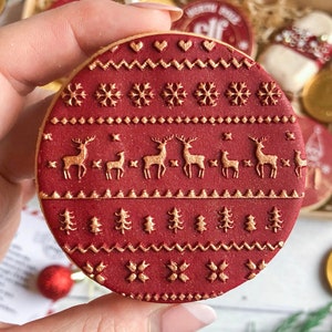 May include: A red and gold Christmas cookie with a snowflake and reindeer pattern. The cookie is decorated with a gold glitter finish.