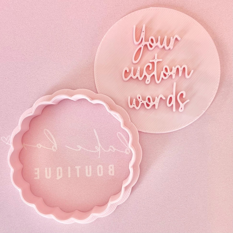 May include: A light pink cookie cutter set. One cutter is round with the words "Your custom words" in a script font. The other is a scalloped circle with the word "Boutique".