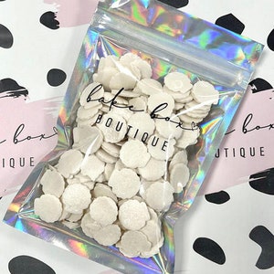 May include: A clear plastic bag filled with white, pearl-like sprinkles. The bag has a label that says "bake box boutique".