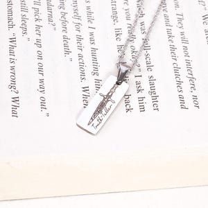 May include: A silver necklace with a rectangular pendant. The pendant displays a sword design and the text "Truth-killer". The necklace is shown on an open book.