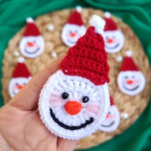 May include: A collection of crocheted snowman ornaments with red hats and white faces. The ornaments are made with yarn and have black eyes, orange noses, and smiling mouths.