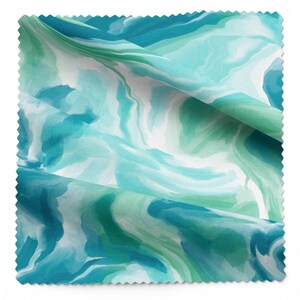 May include: A fabric sample with a watercolour design. The pattern shows swirling shades of teal, turquoise, and white, creating a marbled effect. The fabric is folded, showing the texture and layers of the material.