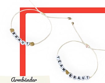 May include: Two white string bracelets with gold beads spelling out "BRAUT" and "TEAM BRAUT".