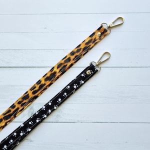 May include: Two fabric keychains with metal clasps. One keychain is black with white paw prints and the other is leopard print.