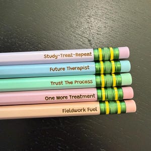May include: Five pastel-colored pencils with metallic green ferrules and yellow bands. The pencils feature brown text: Study~Treat~Repeat, Future Therapist, Trust The Process, One More Treatment, and Fieldwork Fuel, each matching its pencil color.