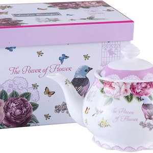 May include: A white porcelain teapot with a floral design and a pink lid. The teapot has a tassel on the handle and is in a pink and white box with the words "The Power of Flower".