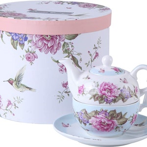 Op de afbeelding: Een bloemig theeservies met een theepot, kop en schotel. De theepot en kop hebben een bloemmotief met roze rozen en vlinders. De schotel is blauw met een bloemmotief. De set wordt geleverd in een witte geschenkdoos met een roze deksel en een bloemmotief.