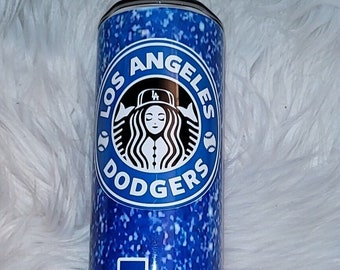May include: A blue and white tumbler with a glitter finish. The tumbler features a Starbucks logo with the words "Los Angeles Dodgers" and a baseball graphic. The LA Dodgers logo is also featured on the bottom of the tumbler.