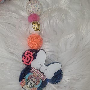 May include: A beaded keychain featuring a San Diego Padres theme. The keychain includes a series of colorful beads, a Padres logo, and a Minnie Mouse-shaped charm with a Dia de los Muertos design and the word "Padres".