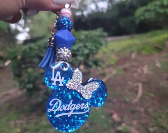May include: Blue and silver glitter keychain with a Mickey Mouse shaped charm. The charm has a butterfly, the letters "LA" and the word "Dodgers" on it.