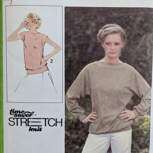 May include: Simplicity sewing pattern number 8886 for a knit top. The pattern is for sizes 12, 14, and 16. The pattern shows a woman wearing a brown top with long sleeves and white pants. The pattern also shows a woman wearing a white top with short sleeves and white pants.