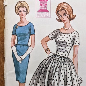 Op de afbeelding: Vintage McCall's naaipatroon voor een jurk met een volle rok of een smalle rok. Het patroon is voor maat 12 met een borstomvang van 81 cm. Het patroon is gedrukt op wit papier met zwarte tekst en illustraties.