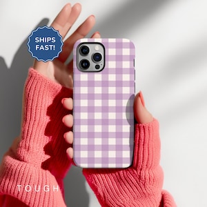 Könnte beinhalten: Eine Handyhülle mit einem lila-weißen Vichy-Muster. Die Hülle wird von einer Person gehalten, die einen rosa Pullover trägt. Die Hülle hat einen Kameraausschnitt und der Text "TOUGH" ist unten im Bild zu sehen. Ein blaues Abzeichen mit dem Text "SHIPS FAST!" ist ebenfalls sichtbar.
